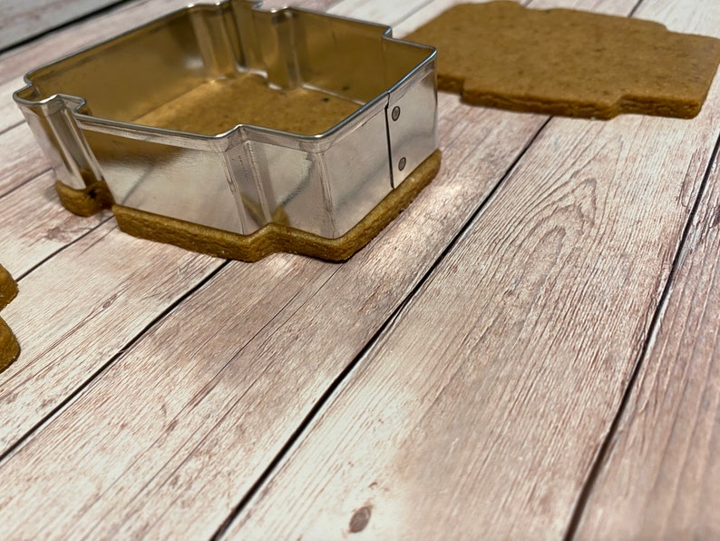 May include: A metal cookie cutter in the shape of a house, with a gingerbread cookie inside.