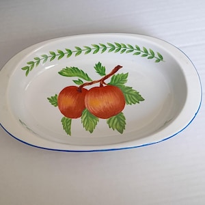 May include: Oval white enamelware serving dish with a blue rim. The dish features a hand-painted design of two red apples with green leaves and a green vine border.