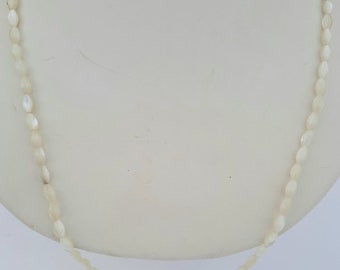 May include: A delicate necklace composed of small, oval-shaped, off-white beads. The beads are strung together to form a single strand, creating a simple yet elegant jewelry piece. The necklace is displayed on a white mannequin bust.