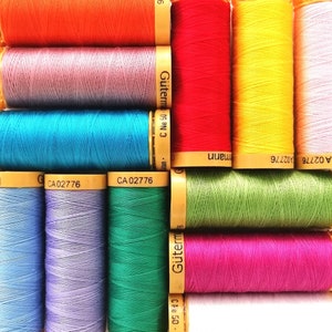 May include: A collection of spools of thread in various colours, including orange, purple, blue, green, yellow, pink, and white. The spools are labelled with the text "Gütermann" and "CA 02776".