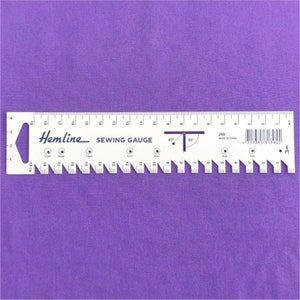 May include: White sewing gauge with black markings and the text "Hemline SEWING GAUGE" and "268 MADE IN CHINA". The gauge has markings for inches and centimetres, as well as a 45-degree and 90-degree angle.