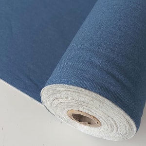 May include: A roll of blue fabric with a white backing. The fabric is tightly rolled and has a textured surface.