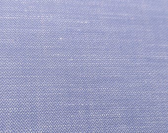 Może przedstawiać: Zbliżenie na jasnoniebieską tkaninę o wyraźnym splocie w jodełkę. Materiał wykazuje spójną diagonalną teksturę stworzoną przez przeplatanie jasnoniebieskich i białych nici, co skutkuje jednolitym wyglądem całej powierzchni tkaniny.