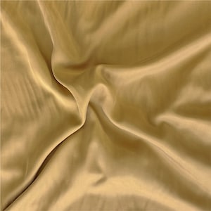 May include: A close-up of a smooth, golden fabric with soft folds and wrinkles. The fabric has a subtle sheen and a luxurious feel.