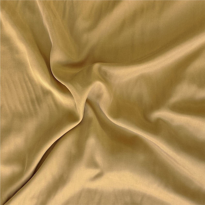 May include: A close-up of a smooth, golden fabric with soft folds and wrinkles. The fabric has a subtle sheen and a luxurious feel.