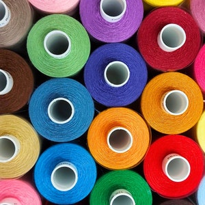 May include: A collection of colourful spools of thread, each with a different colour and a white label with text. The spools are arranged in a circle, with the labels facing outwards.