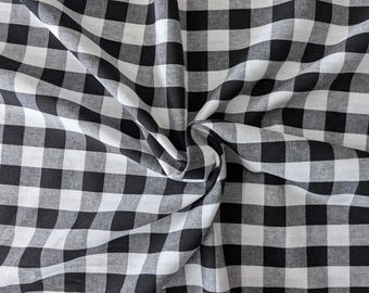 Może przedstawiać: Tkanina w klasyczny czarno-biały wzór w kratkę gingham. Materiał jest ułożony w miękkie fałdy i marszczenia, tworząc teksturowaną powierzchnię, która podkreśla powtarzający się wzór kwadratowej siatki na całej powierzchni materiału.