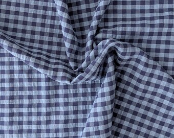 May include: A piece of fabric featuring a classic gingham pattern with alternating squares of dark navy blue and light gray. The material is draped to show folds and creases, highlighting the consistent checkered design across the surface.