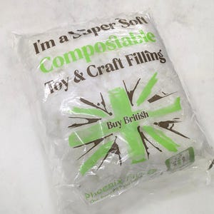 May include: A transparent plastic bag containing white, soft filling material. The bag features green and brown text and graphics, including the words "I'm a Super Soft Compostable Toy & Craft Filling" and "Buy British."