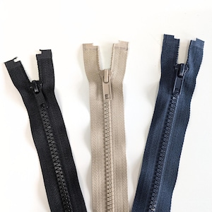 May include: Three zipper closures in black, beige, and navy blue. The zippers are open and ready to be sewn into a garment or project.