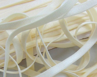 May include: A close-up of a pile of ivory-colored elastic trim. The trim is flat and has a subtle sheen.