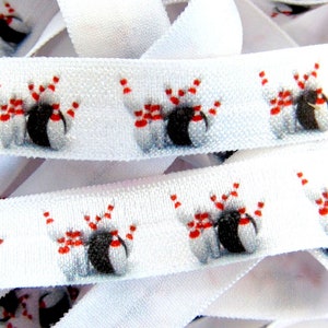 以下が含まれることがあります： 白の伸縮性リボン。黒、白、赤のボーリングピンとボーリングボールの繰り返し模様。リボンは丸められており、緩いストランドでも表示されています。