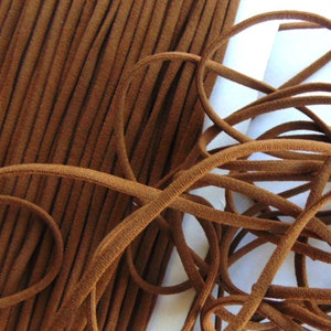 May include: Close-up of brown elastic cord, both coiled and in a neat stack. The cord appears to be made of a soft, suede-like material. The colour is a warm, medium brown, and the texture is slightly fuzzy. The cord is likely used for crafting or sewing projects.