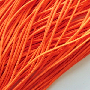 May include: A close-up shot of a collection of bright orange elastic cord. The cords are densely packed, forming a textured surface. The vivid colour and close arrangement suggest a craft material, suitable for various projects.