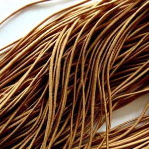 May include: Close-up of a pile of tan elastic cord. The cords are densely packed, forming a textured surface. The thin, flexible cords are suitable for various crafting and jewellery-making projects.