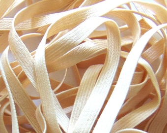 May include: A close-up of a pile of beige elastic, also known as stretch band or shirring elastic. The elastic is soft and flexible, and it is perfect for sewing projects.