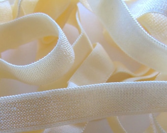 May include: Close-up of a pile of ivory-colored elastic ribbon. The ribbon is soft and flexible, with a slightly textured surface. The ribbons are intertwined and create a sense of depth and texture. Ideal for sewing and crafting projects.