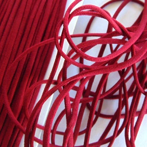 May include: A close-up shot of burgundy elastic cord. The cord is neatly stacked on the left and tangled on the right. The deep red cord has a smooth texture. The background is white.