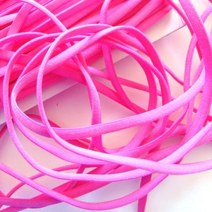 May include: Vibrant pink elastic cord, arranged in a tangled heap. The cord is smooth and flexible, with a rounded shape. The bright pink colour suggests a craft or sewing material, possibly for clothing or accessories.