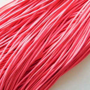 May include: A close-up shot of a mass of bright pink elastic cord. The cords are densely packed, forming a textured surface. The colour is a vibrant, solid pink, and the cords appear smooth and flexible. Suitable for various craft and sewing applications.
