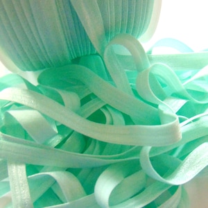 May include: A close-up of a spool of light blue elastic ribbon. The ribbon is soft and stretchy, and it is perfect for adding a touch of color and texture to your crafts.