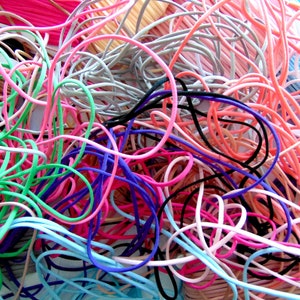 May include: A jumbled pile of colourful elastic cords. The cords are in shades of pink, green, blue, purple, black and white.