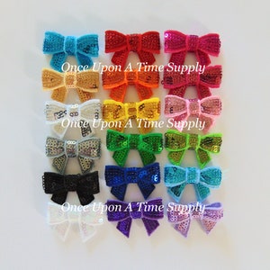 May include: Assortment of 18 small sequined bows in various colours, including turquoise, red, orange, yellow, pink, silver, green, gold, black, blue, white, purple, and lavender.  "Once Upon A Time Supply" is printed on the white background.
