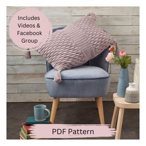 May include: A PDF pattern for a crocheted pillow with a textured design. The pillow is a light purple color and has tassels on each corner. The pillow is sitting on a blue armchair with wooden legs. The text "PDF Pattern" is written on a pink background.