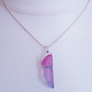May include: A silver necklace with a pendant featuring a pink and purple crystal. The crystal is a long, irregular shape, with a silver metal frame. The chain is a thin, silver snake chain.