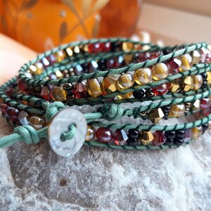 May include: A multi-strand wrap bracelet with green leather cord, gold, black, and red beads, and a silver button closure.