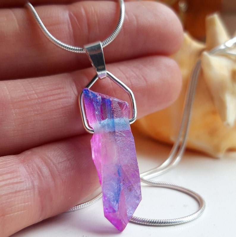 May include: A colourful crystal pendant necklace. The crystal, approximately 3.8 cm long, displays pink, purple, and blue shades, held by a silver-toned metal setting and chain. The necklace is a striking piece of jewellery.