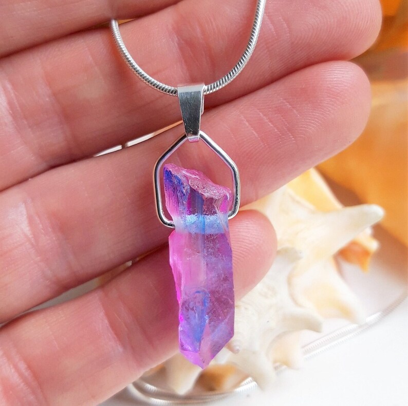 May include: A silver necklace with a multi-coloured crystal pendant. The crystal has pink, purple, and blue hues, with a raw, natural texture. The pendant hangs from a delicate silver chain, creating a striking contrast. A unique piece of jewellery.
