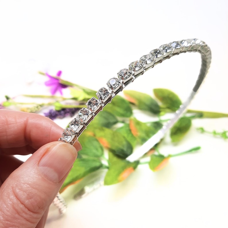 May include: A silver headband with clear rhinestones. The headband is flexible and has a simple design.