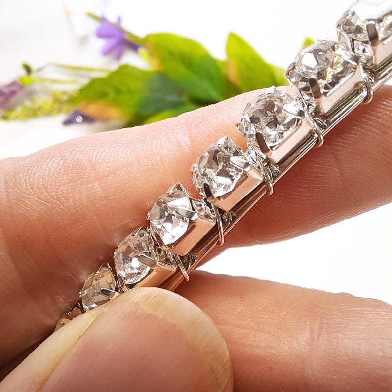 May include: A silver chain bracelet with clear rhinestones. The bracelet is made of small, round rhinestones that are set in a silver metal chain.
