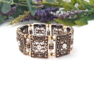 May include: A gold-toned stretch bracelet with a filigree design and clear crystal accents.