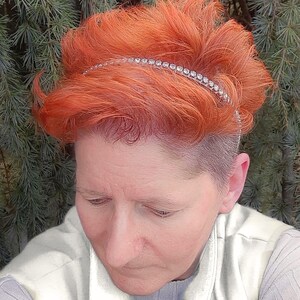 May include: A woman with short, bright orange hair is wearing a silver headband with rhinestones. The headband is thin and sits just above her forehead.