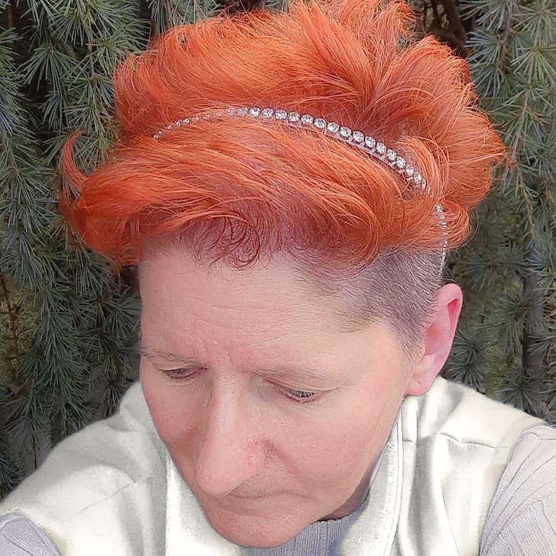 May include: A woman with short, bright orange hair is wearing a silver headband with rhinestones. The headband is thin and sits just above her forehead.