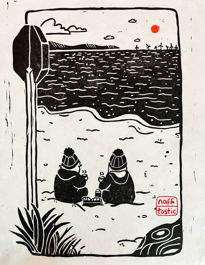 Linoprint of two wild swimmers enjoying pastries on the beach. Printed in black ink with a red sun.