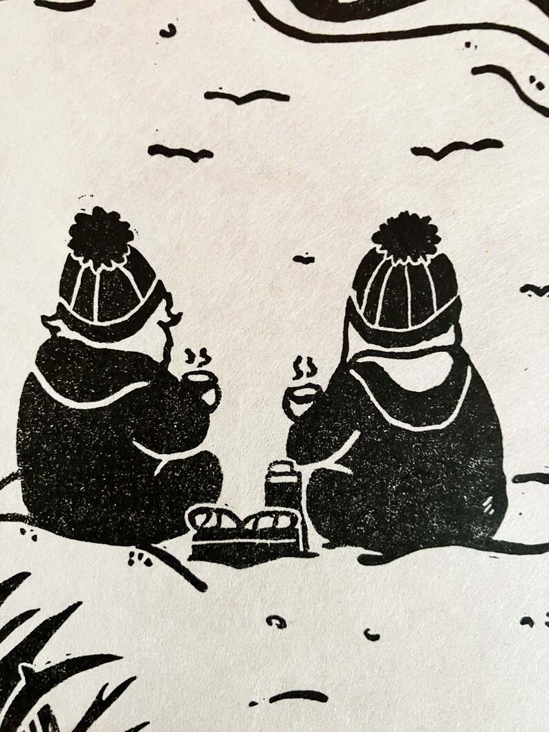 Linoprint of two wild swimmers enjoying pastries on the beach. Close up of wild swimmers. Printed in black ink with a red sun.