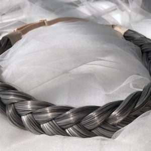 May include: A braided hair extension made of gray human hair, with a brown elastic band for attaching it to the hair.