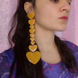 May include: A pair of long, yellow heart-shaped earrings. The earrings are made of multiple hearts stacked on top of each other, creating a cascading effect.