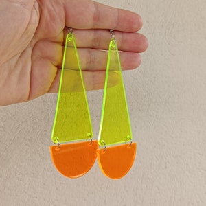 Op de afbeelding: Een paar neon groene en oranje acryl oorbellen. De oorbellen zijn driehoekig van vorm met een halve cirkel aan de onderkant.