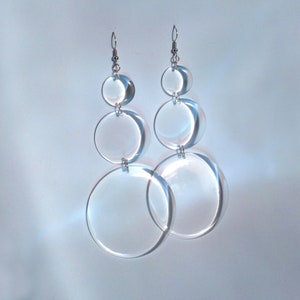 May include: A pair of clear acrylic earrings with three graduated circles on each earring. The earrings are suspended from silver hooks.