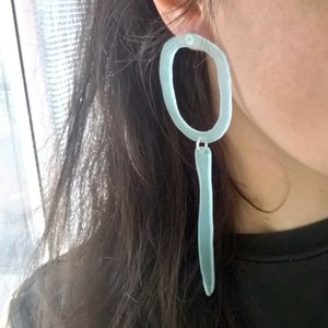 May include: A pair of translucent blue earrings with a long, thin, teardrop-shaped dangle and a larger oval hoop at the top.