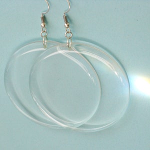 May include: A pair of clear oval-shaped earrings with silver hooks. The earrings are made of glass and have a slight rainbow effect.