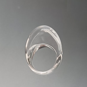 Puede incluir: Un anillo de cristal transparente con una forma redonda y lisa. El anillo es grueso y tiene una banda ancha.