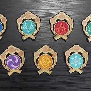 Könnte beinhalten: Acht gestickte Aufnäher mit verschiedenen farbigen Designs. Jeder Aufnäher zeigt ein kreisförmiges Design mit einem goldenen Rand und einem goldenen Band am unteren Rand. Die Designs umfassen eine blaue Welle, einen grünen Vogel, eine rote Flamme, ein grünes Herz, einen violetten Wirbel, einen orangefarbenen Wirbel, eine blaue Schneeflocke und einen gelben Wirbel.