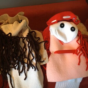 May include: Two sock puppets, one brown with long brown yarn hair and a white face, the other white with red yarn hair and a pink face, with black button eyes.