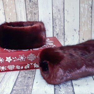 May include: A set of two burgundy faux fur arm warmers and a headband. The arm warmers and headband are made of soft, plush faux fur. The arm warmers are approximately 25 cm long and the headband is about 15 cm wide.