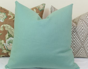 May include: Four decorative throw pillows in various patterns and colors. The front pillow is a solid light teal color. Other pillows feature floral and geometric designs in brown, white, and green.